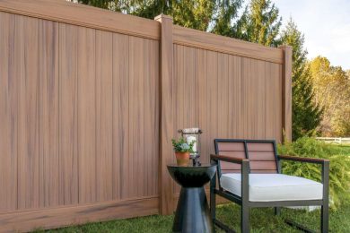 a small table and chair resting against a faux wood vinyl fence in a backyard